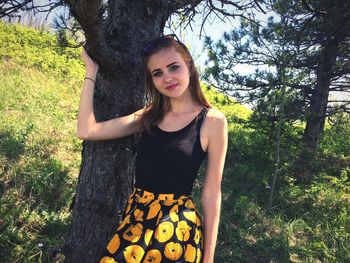 Portrait of beautiful young woman standing by tree in park