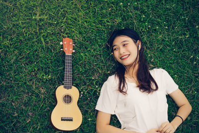 Smiling young woman listening music by ukulele on grass