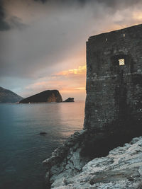 Old building by sea against sky during sunset