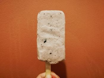 Close-up of hand holding ice cream against orange background