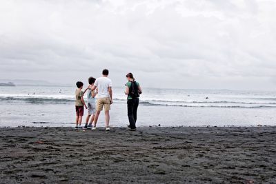 Family standing on shore at beach against sky