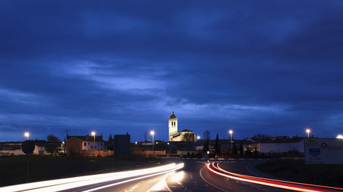 Light trails on road amidst buildings against sky at night