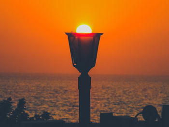 Illuminated lamp by sea against orange sky