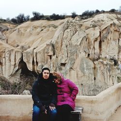 Portrait of couple sitting on bench against mountain