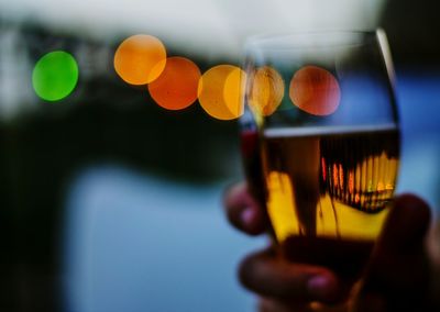 Close-up of hand holding wine glass against blurred lights