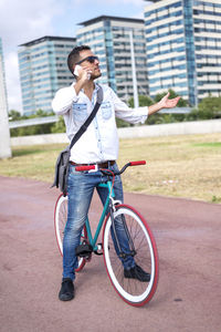 Mid adult man with bicycle talking on mobile phone while standing against buildings
