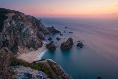 Rocks in sea against sky during sunset