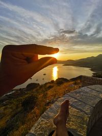 Midsection of person by sea against sky during sunset