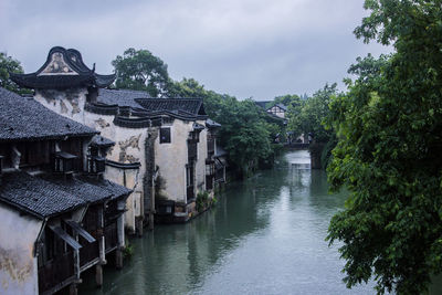 Houses by river amidst buildings against sky