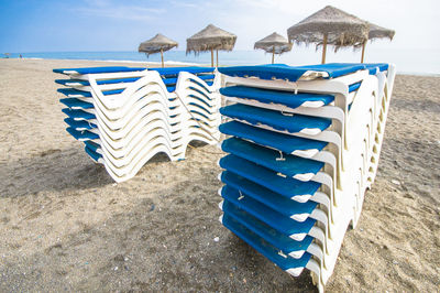 Deck chairs on sand at beach against blue sky