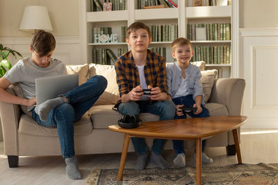 Three brother boys playing computer games on a laptop and video games with joysticks in their hands