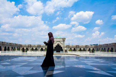 Woman standing with arms outstretched against cloudy sky