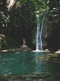 Man sitting by waterfall in forest