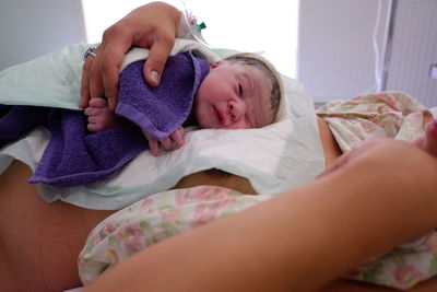 New born baby laying on mother's belly holding her finger