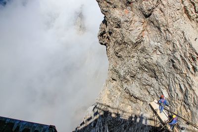 Workers on wooden plank by rocky cliff