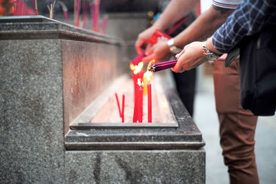 Midsection of man holding burning candles against temple