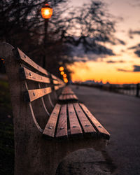 Empty benches in row against sky at sunset