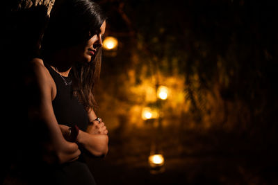 Portrait of young woman looking at illuminated camera at night