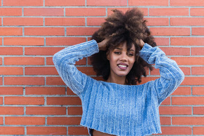 African american woman smiling with long afro hair posing while touching her hair in brick wall. 