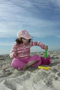 Full length of girl playing with sand pail and shovel at sandy beach