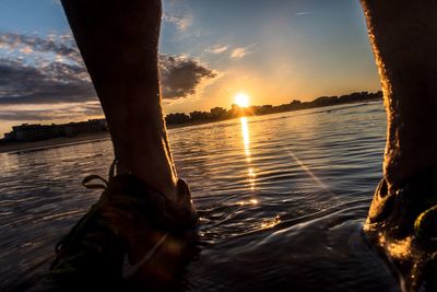 Low section of people on sea at sunset
