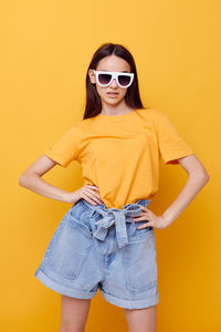 Young woman wearing sunglasses while standing against yellow background