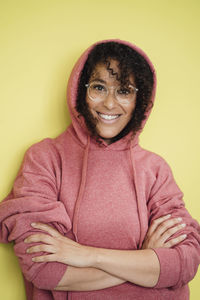 Happy mature woman with arms crossed in front of yellow wall