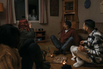 Terrified multiracial friends looking at ghost through window in log cabin