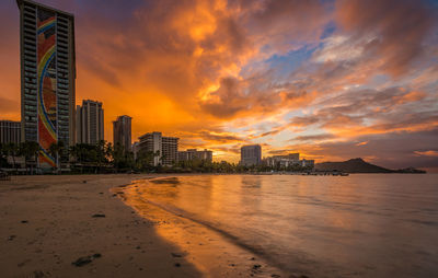 Sea by buildings against sky during sunset