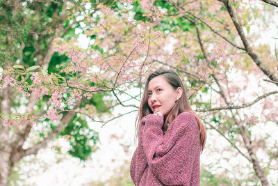 Mid adult woman wearing sweater while standing against cherry tree
