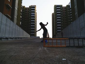 Full length side view of girl skating on concrete amidst buildings in city