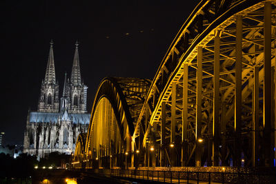 Illuminated bridge by buildings against sky at night