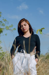 Beautiful young woman standing on field against sky