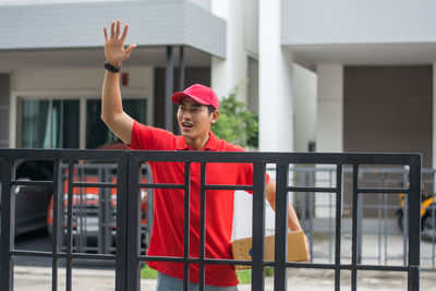 Delivery man standing at closed gate against buildings