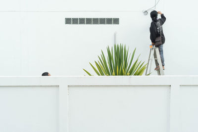 Rear view of mature woman standing on ladder against wall