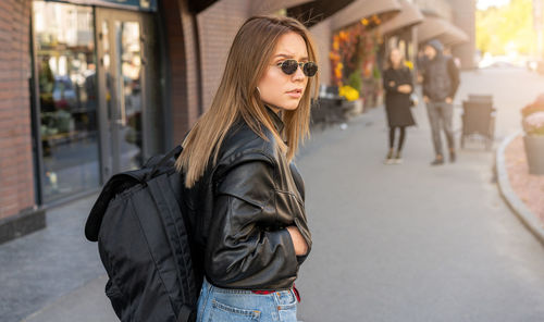 Portrait of young woman wearing sunglasses standing on street in city
