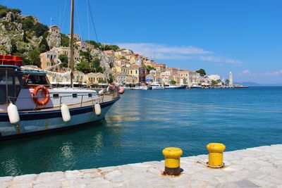 Sailboats moored on sea by city against sky