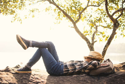 Side view of boy lying on fallen tree against sky