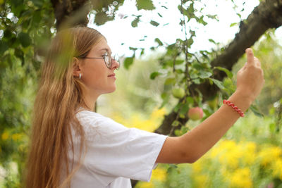 Portrait of young woman looking away while standing against trees