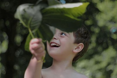 Close-up of smiling shirtless boy holding plants