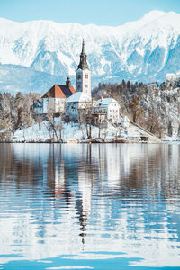 Buildings by lake against mountain during winter