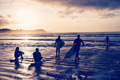 Silhouette people on beach against sky during sunset