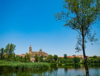 Lake and buildings against clear blue sky