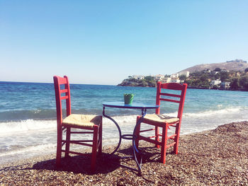 Chairs on beach against clear blue sky