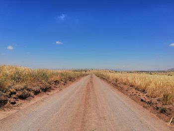 Dirt road amidst land against sky