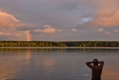 Low section of man by lake against rainbow in the sky