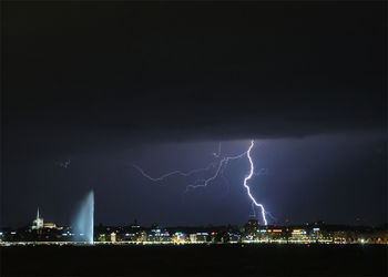 Lightning over illuminated cityscape against sky at night