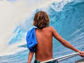 Rear view of shirtless boy in sea against sky