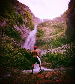 Rear view of man standing on rock against waterfall