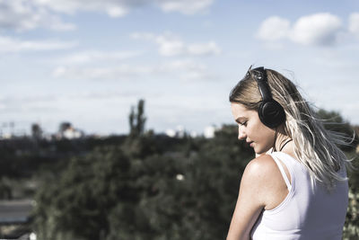 Young woman listening to music against sky